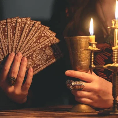 Cartes de tarot, coupe dorée et bougie sur une table, mains avec des bagues.